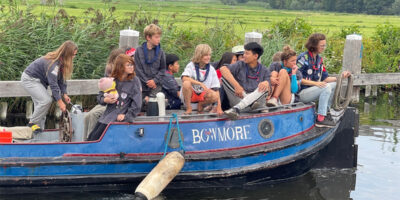 Kinderen en leiding van De Lodewijksgroep varen samen in een boot tijdens waterscouting in Leiden