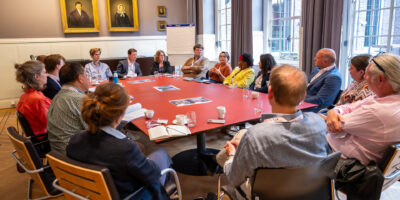 Een groep mensen in een cirkel rond een tafel. Ze nemen deel aan de denktank.