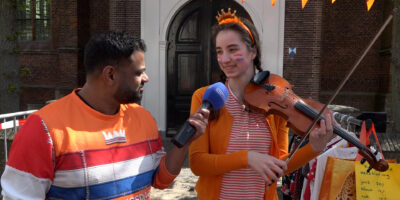 Rudo praat met een meisje dat viool speelt op de vrijmarkt in Leiderdorp tijdens Koningsdag in de regio