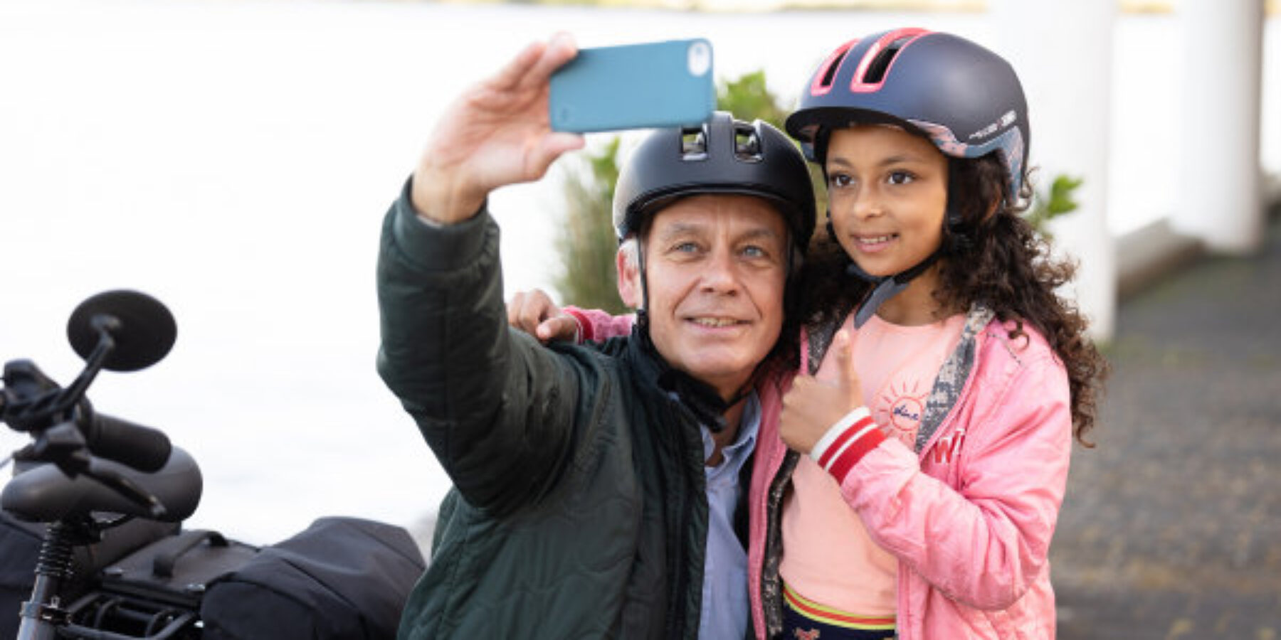 Een man maakt een foto met een kind. Ze dragen beide een fietshelm. VVN pleit voor meer gebruik fietshelm in Nederland