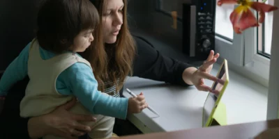 Moeder houdt haar kind vast terwijl ze op haar tablet zit.