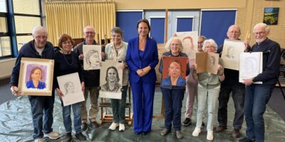 Burgemeester Nadine Stemerdink is geportretteerd door een groep tekenaars en schilders. De burgemeester staat op de foto met deze mensen en de portretten.