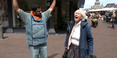 Rudo! op de Leidse markt aflevering 134. Rudo spreekt met een mevrouw die zware tassen draagt.