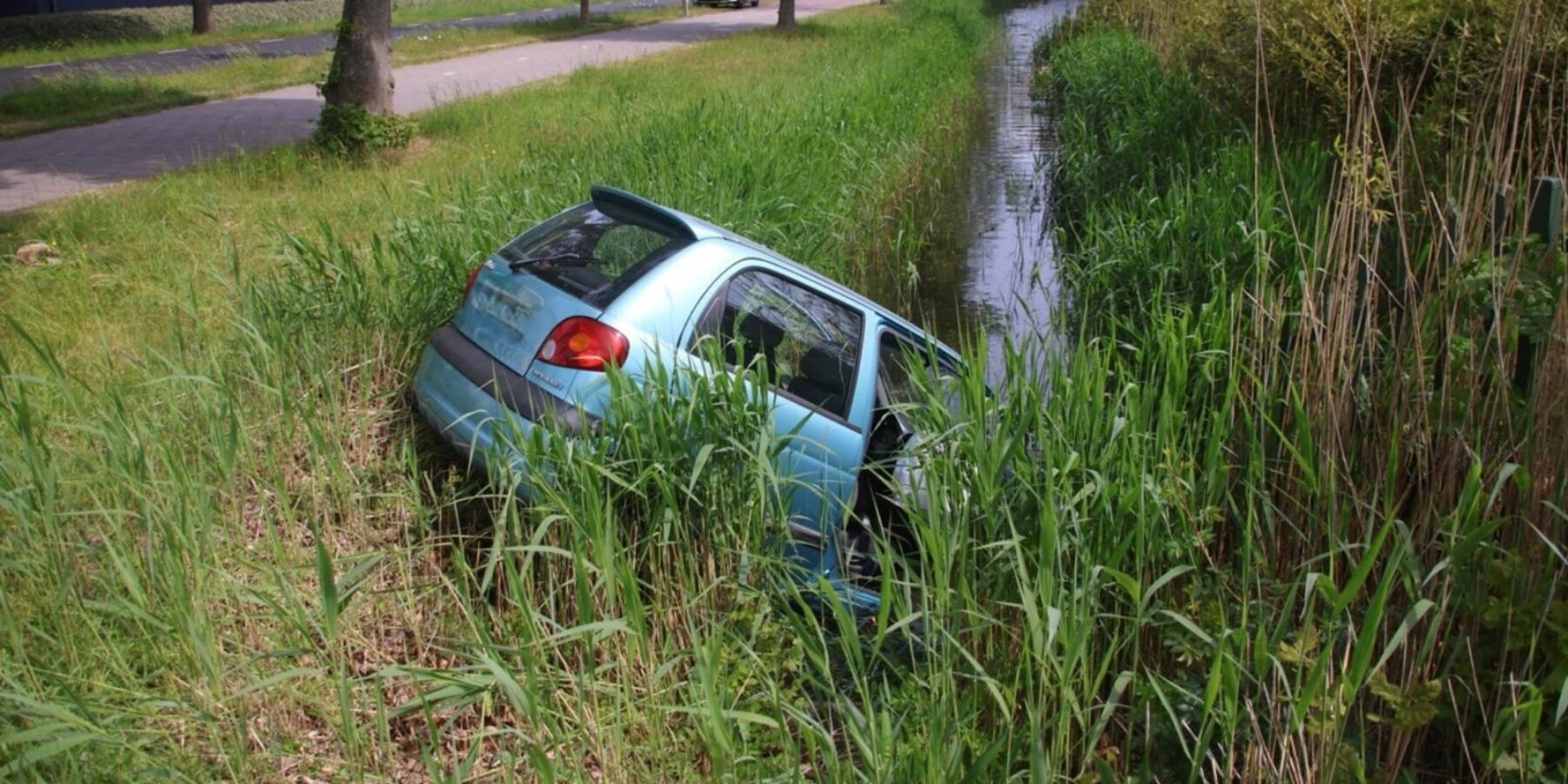 Auto in het water langs de Haarlemmerstraatweg in Oegstgeest. Omstanders schoten te hulp.