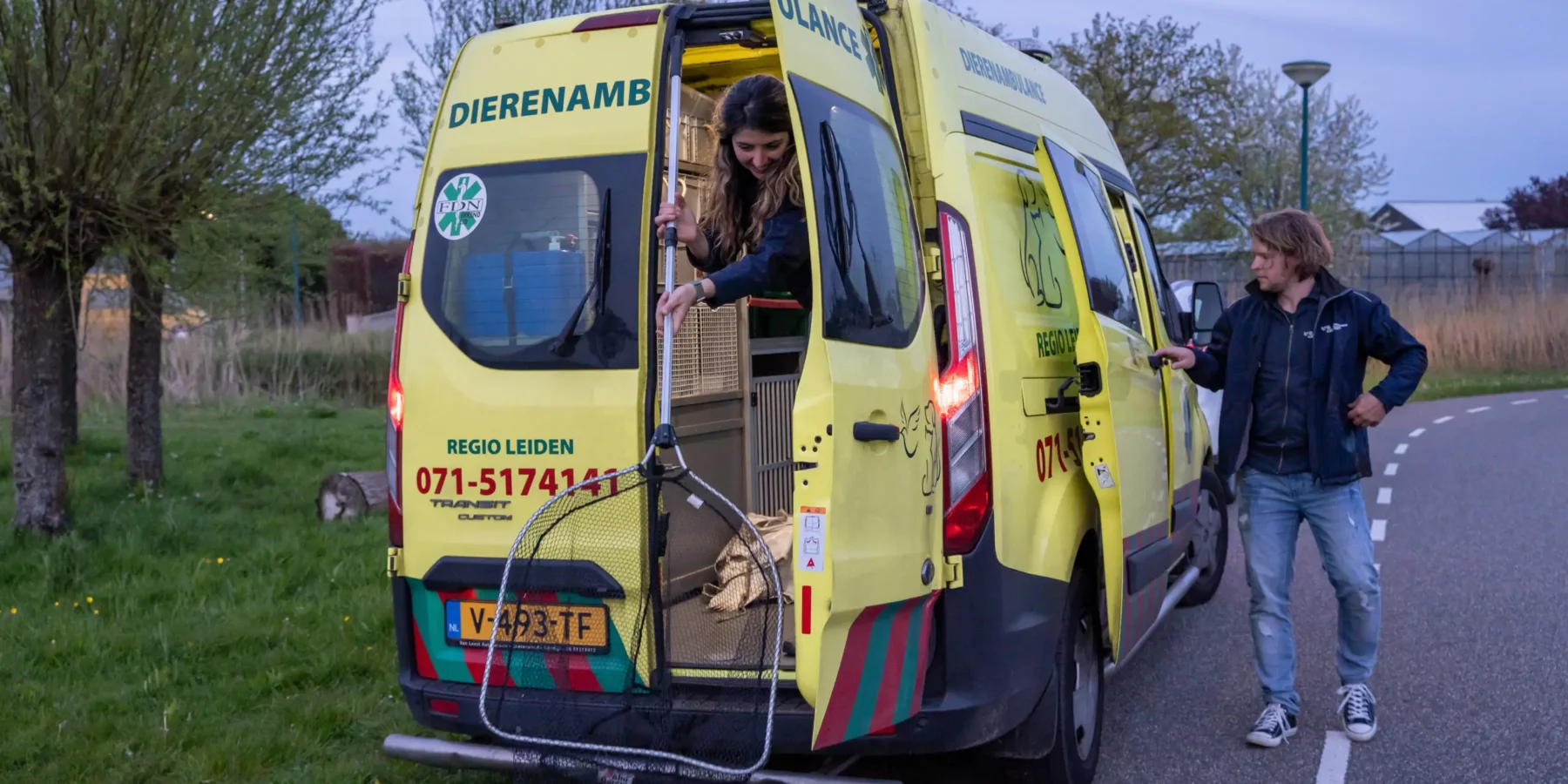 De dierenambulance met twee vrijwilligers, waarvan er een net vasthoudt.