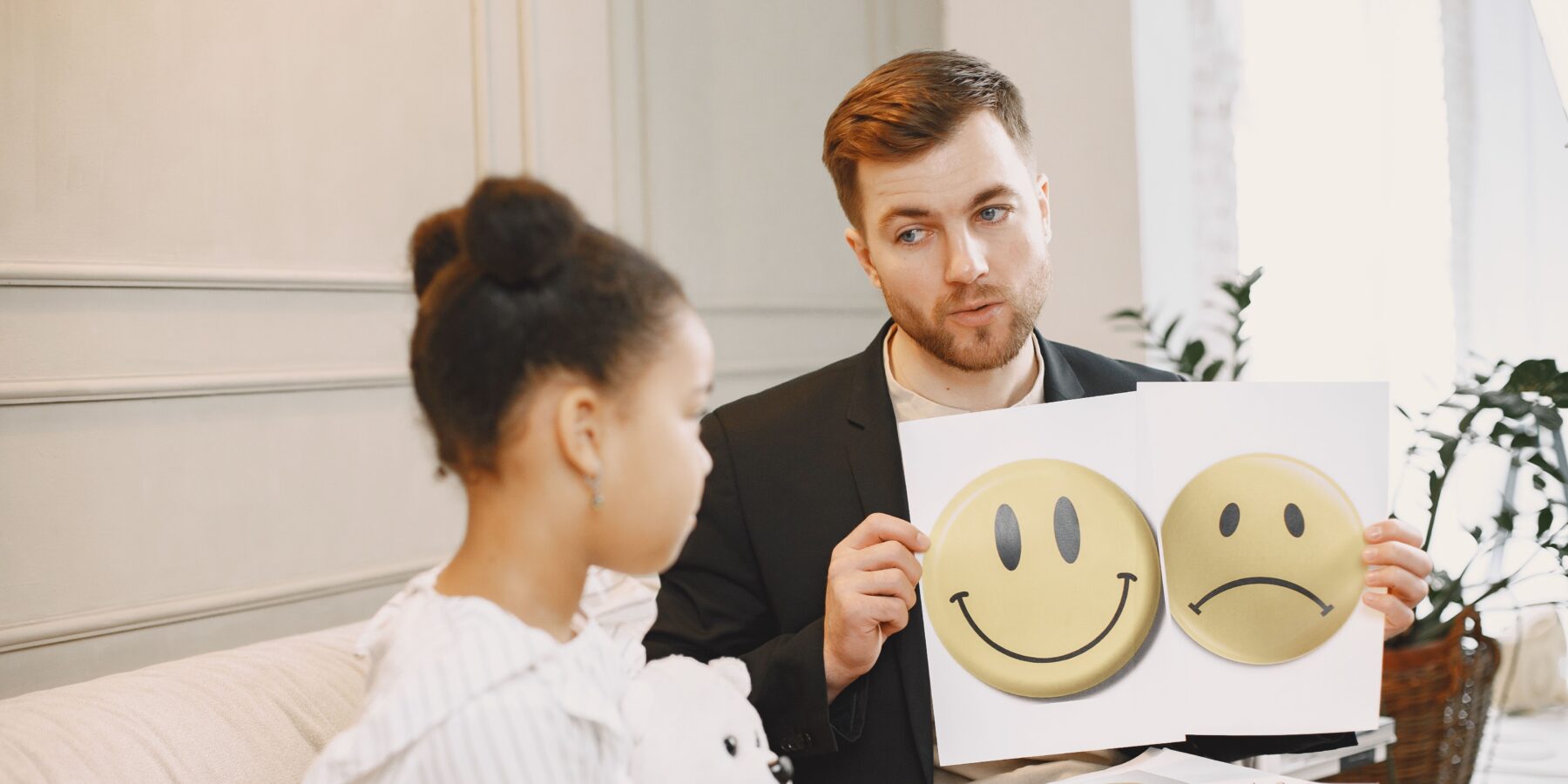 Een kind krijgt van een geestelijke hulpverlener twee plaatjes te zien van een lachende en een sombere smiley te zien.