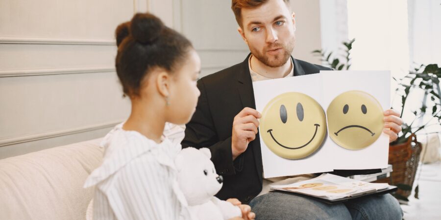 Een kind krijgt van een geestelijke hulpverlener twee plaatjes te zien van een lachende en een sombere smiley te zien.
