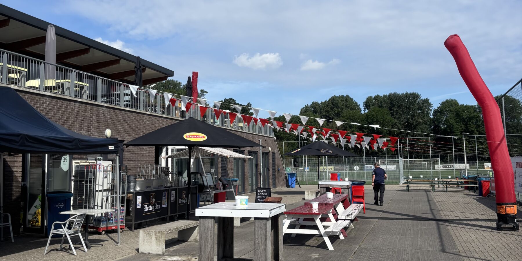 Clubgebouw van RCL in Leiderdorp met terras, rood-witte vlaggen en sportvelden op de achtergrond.