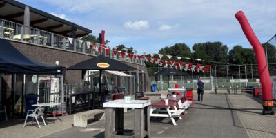 Clubgebouw van RCL in Leiderdorp met terras, rood-witte vlaggen en sportvelden op de achtergrond.