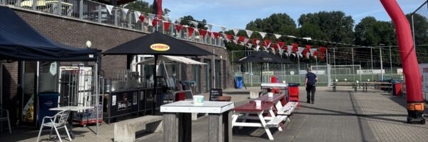 Clubgebouw van RCL in Leiderdorp met terras, rood-witte vlaggen en sportvelden op de achtergrond.
