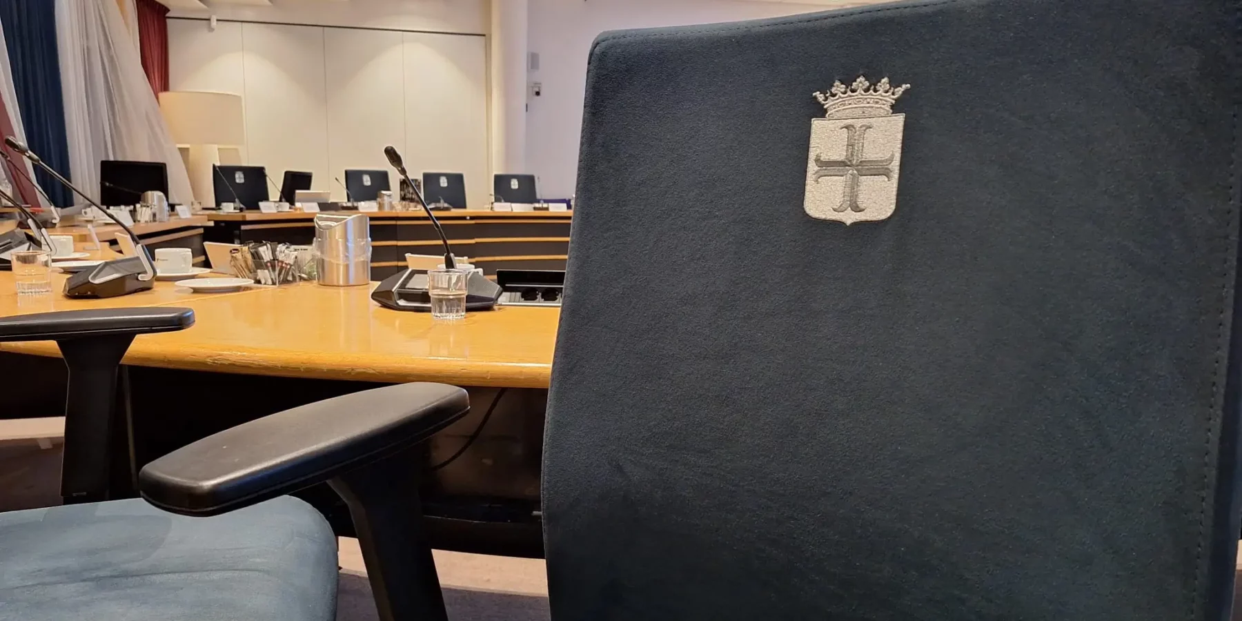 De raadszaal in Oegstgeest waarin vooral een stoel in de zaal is gefotografeerd. Op de achtergrond is een microfoon te zien.