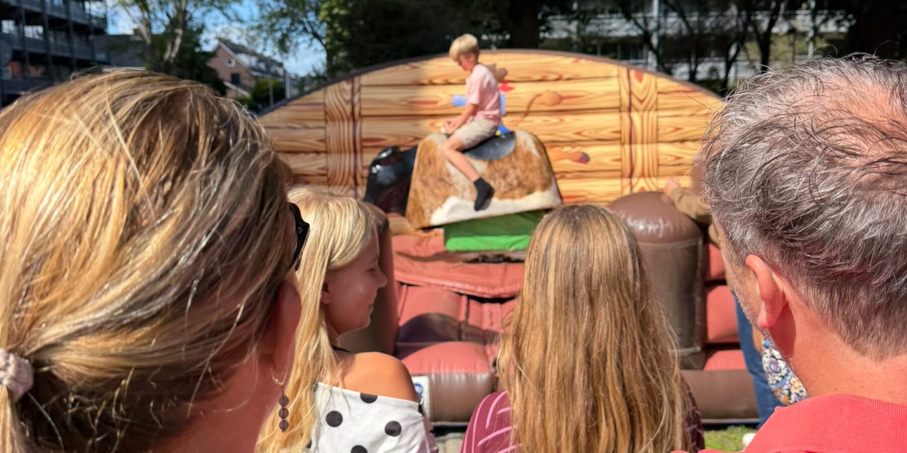 Publiek kijkt toe hoe een jongen op de rodeostier zit op de jaarmarkt in Leiderdorp.