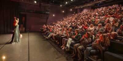 Theater Ins Blau met een artiest op het podium en publiek in de theaterzaal.